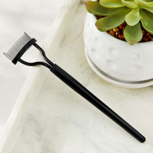 Eyelash separator tool with black handle and white comb teeth on tabletop
