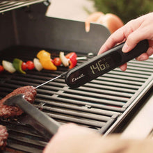 Infrared surface thermometer with folding probe held over grill grate for reading