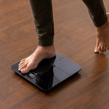 Smart fitness scale with LCD display under bare feet on a dark platform