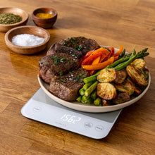 Kitchen digital scale with LCD display under a plate of cooked food and vegetables