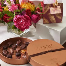 Open round chocolate tin with assorted chocolates and a closed gift box