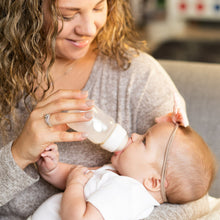 Mother feeding baby with clear standard-neck bottle and white nipple