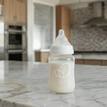 Clear glass baby bottle with white nipple, filled with light milk, Evenflo logo
