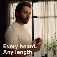 Man holding a beard softening butter jar with black lid and aged bourbon label