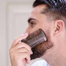 Ebony wood beard comb held to a man’s beard, dual row teeth visible