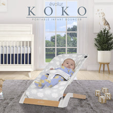 Portable infant bouncer with light gray cloud-pattern seat holding a baby, white frame