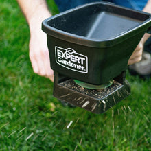 Handheld broadcast spreader dispensing granules over lawn grass