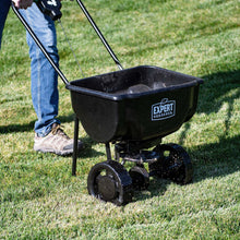 Black push broadcast spreader being pushed with hopper and Expert Gardener label