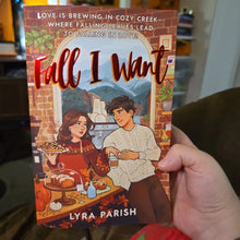 Hand holding paperback romance novel with illustrated autumn cafe cover