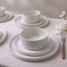 White stoneware bowls and plates stacked, with a center bowl