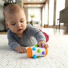 Sensory roller rattle toy held by a baby, with orange end, blue wheels, green and purple