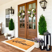 Faux cedar topiary trees in black pots, placed by a front door mat area