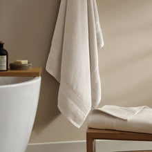 Cream bath towel set, one towel draped and one folded on a bathroom ledge