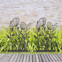 Black metal flower garden stakes with leaf and blossom cutouts, standing on grass