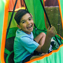 Child smiling inside a green tented saucer swing with orange trim and black straps.