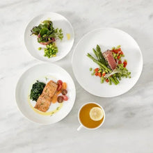 Coupe dinnerware set with plates and cups, white ceramic, on table with food