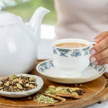 Cup of chai with floral teacup and saucer beside bowls of loose leaf tea