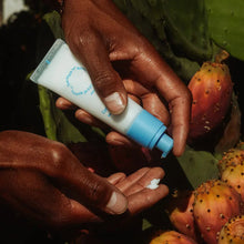 Hand holding blue-capped hand cream tube with white cream on fingers