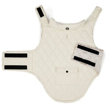 Cream sleeveless quilted dog coat with sherpa pocket trim and black strap tabs.