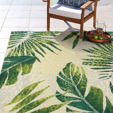Indoor/outdoor rug with large green leaf motifs on cream background, angled view.