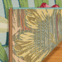 Indoor/outdoor rug corner detail with woven texture and yellow flower on blue-green