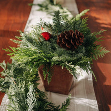 Evergreen centerpiece in wooden box with pinecones, red ornament, on white table runner