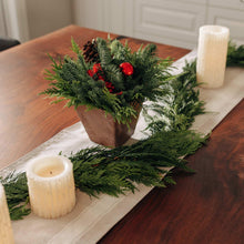 Holiday evergreen centerpiece in wooden tray with red berries, pinecones, and two white candles
