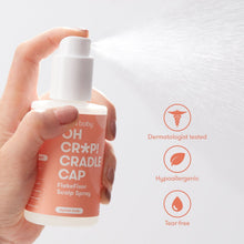 Cradle cap treatment spray bottle held in hand with orange label and icons