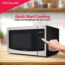 Stainless steel microwave on countertop with keypad and hand pressing start button