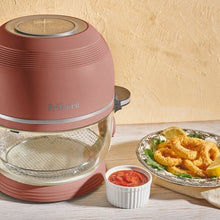 Fritaire pink air fryer with clear bowl and mesh rack, beside a plate of food