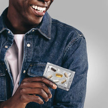 Men's multivitamin blister pack held in hand by smiling man in denim jacket