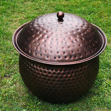 Dark copper hammered hose storage pot with domed lid on green grass