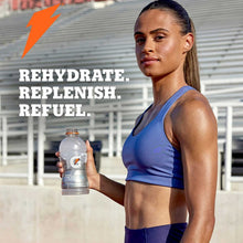 Sports drink bottle held by athlete in blue tank top, outdoors setting