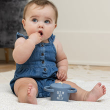 Baby sitting with hand in mouth next to light blue snack cup, 'GET IN MY BELLY'.
