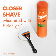 Manual razor with black handle and orange 5-blade head, with shaving gel bottle nearby