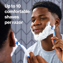 Shaving razor in use with blue cartridge and white handle, with shaving lather.