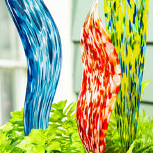 Close-up of glass garden stakes: blue, red, and yellow swirled glass on black stems.