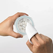 Baby food glass container held open by hands, showing white contents