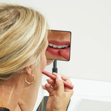 Adjustable LED mirror in use for applying lipstick; LED-lit face reflection