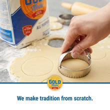 Hand pressing a biscuit cutter into flour dough rounds on tray