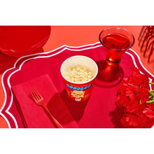 Microwaveable mac and cheese cup with cheese inside, with fork, spoon, and glass