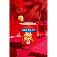 Microwaveable mac and cheese cup with red lid, beside glass jug and utensils