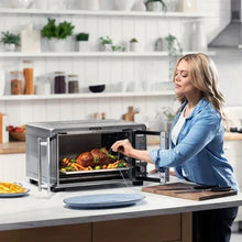 Stainless steel countertop air fryer oven on kitchen counter with door open and food cooking.