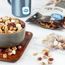 Trail mix in metal bowl with scattered nuts and dried fruit; sealed pouch nearby
