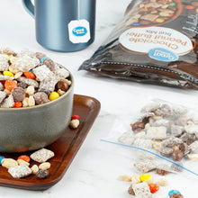 Trail mix in a bowl with candy-coated pieces and nuts beside an open pouch