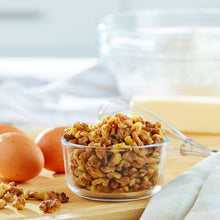 Chopped walnuts in a small glass bowl with scattered walnut pieces
