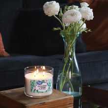 Eucalyptus + sage scented candle with lit wicks in clear jar on wooden surface