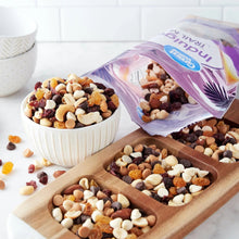 Trail mix in bowls with nuts, raisins, and cereal pieces next to open bag