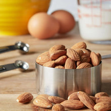Bowl of whole almonds with almonds scattered on wooden table