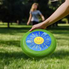 Green flying disk toy held in hand, blue smiling sun center